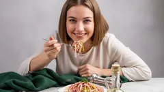 Usmívající se žena jí špagety u stolu s kořením v moderním prostředí.