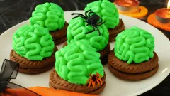 Halloweenské sušenky s mozkem, zelený krém a dekorace pavouci na bílém talíři