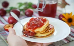 Lívance s domácí švestkovou marmeládou na talíři, čerstvé švestky v pozadí.