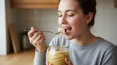 Žena jí pudink lžící z průhledné sklenice v domácím prostředí.