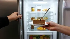 Dort na talíři před otevřenou lednicí s potravinami, ruce drží talíř i dveře ledničky.