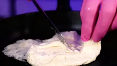 Smažená vaječná omeleta krájená nožem na pánvi, ruka v růžové rukavici.